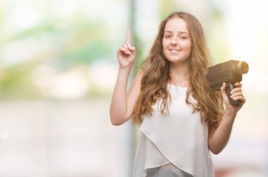 Bir fikir ya da soru işaret parmağı ile gülen yüz, bir numara süper 8 video kamera tutan genç sarışın kadın şaşırttı