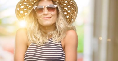 Genç kadın yaz şapka düşünme ve şüphe ve merak ifade seyir güneş gözlüğü kullanarak