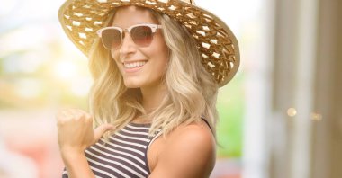 Genç kadın yaz şapka gurur, heyecanlı ve küstah, güneş gözlüğü kullanarak zafer yüzü ile işaret