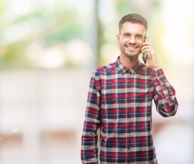 Genç yenilikçi yetişkin adam ayakta ve diş gösterilen kendine güvenen bir gülümsemeyle gülümseyerek mutlu bir yüz ile telefonda konuşurken