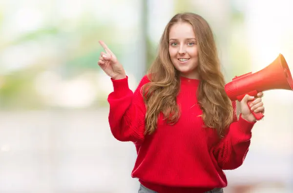Νεαρή Ξανθιά Γυναίκα Κρατώντας Κόκκινα Μεγάφωνο Πολύ Χαρούμενος Δείχνοντας Χέρι — Φωτογραφία Αρχείου