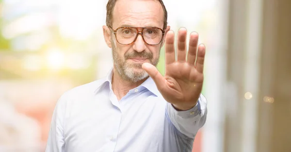 Middle age man with glasses annoyed with bad attitude making stop sign with hand, saying no, expressing security, defense or restriction, maybe pushing