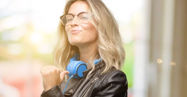 Young student woman with headphones proud, excited and arrogant, pointing with victory face