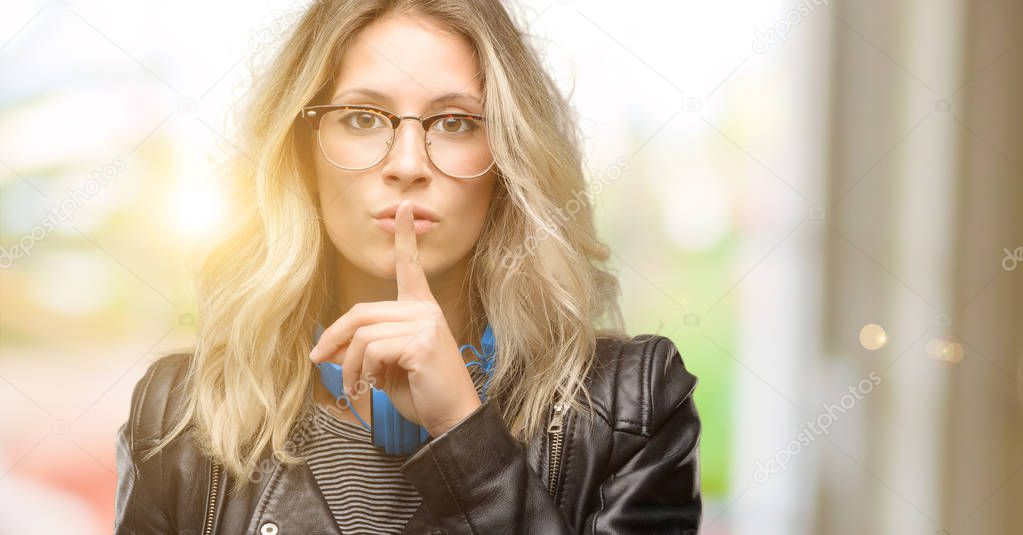 Young student woman with headphones with index finger on lips, ask to be quiet. Silence and secret concept