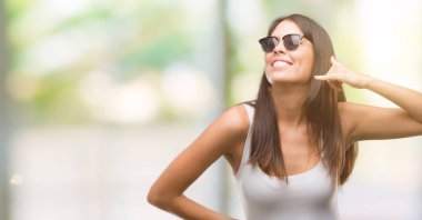 Genç güzel İspanyol yapıyor gülümseyen güneş gözlüğü takıyor telefon hareketi ile el ve parmak telefonda konuşuyor gibi. Kavramları iletişim.