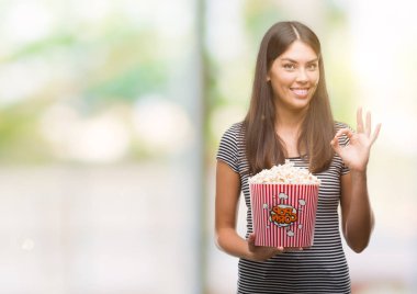 Genç güzel İspanyol parmak, mükemmel sembolü ile ok işareti yapıyor patlamış mısır yemek