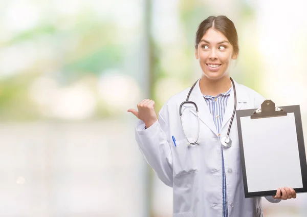 Jovem Hispânico Médico Mulher Segurando Prancheta Apontando Mostrando Com Polegar — Fotografia de Stock