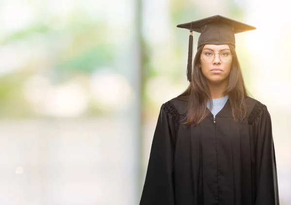 若いヒスパニック系女性の顔に卒業キャップと真剣な表情で制服を着ています シンプルで自然なカメラを見てください — ストック写真