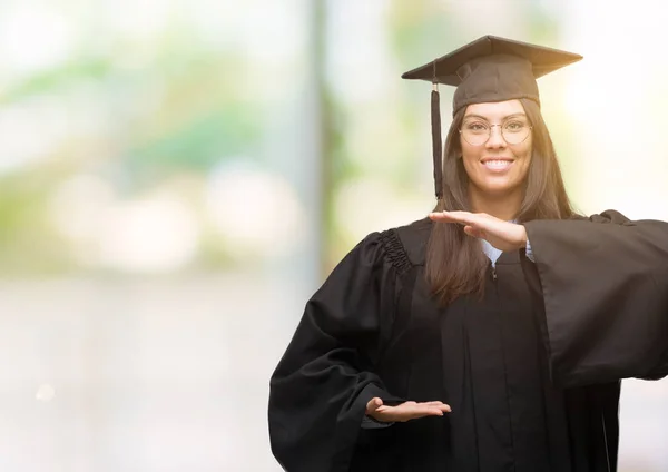 年轻的西班牙裔妇女穿着毕业帽和统一手势与手显示大和大尺寸标志 测量符号 微笑着看着相机 测量概念 — 图库照片