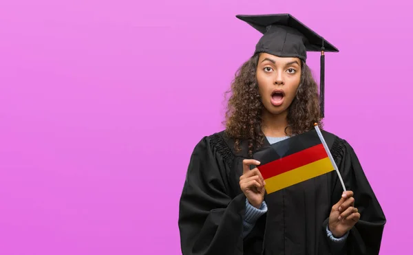 Mujer Hispana Joven Vistiendo Uniforme Graduación Sosteniendo Bandera Alemania Asustada —  Fotos de Stock