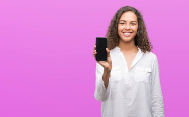 Ayakta ve diş gösterilen kendine güvenen bir gülümsemeyle gülümseyerek mutlu bir yüz ile akıllı telefon kullanan genç İspanyol kadın