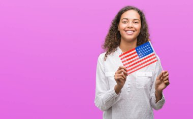 Estates Amerika bayrağı ile ayakta ve diş gösterilen kendine güvenen bir gülümsemeyle gülümseyerek mutlu bir yüz tutan genç İspanyol kadın