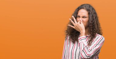 Beautiful young hispanic woman smelling something stinky and disgusting, intolerable smell, holding breath with fingers on nose. Bad smells concept. clipart