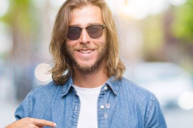 Kendisi için sürpriz yüz işaret parmağı ile smartphone kullanarak ileti gönderme izole arka plan üzerinde uzun saçlı yakışıklı delikanlı