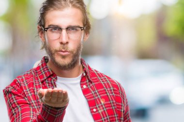 Genç yakışıklı adam uzun saçlı gözlüklü bir öpücük el ile güzel ve seksi olmak hava üfleme kamera bakarak izole arka plan üzerinde. Aşk ifade.