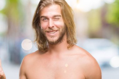 Genç yakışıklı gömleksiz adam uzun saçlı seksi vücut ile mutlu yüz zafer işareti yaparken kameraya göz kırpıyor gülümseyen izole arka plan üzerinde gösterilen. İki numaralı.