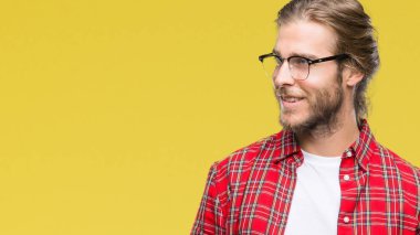 Genç yakışıklı adam uzun saçlı gözlüklü uzak tarafına yüzünde, doğal ifade gülümseme ile seyir izole arka plan üzerinde. Kendine güvenen gülüyor.