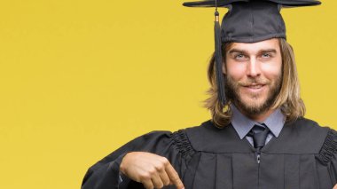 Genç yakışıklı adam uzun saçlı yüzünde gülümseme ile kendinden emin görünüyorsun, kendini gururlu ve mutlu parmakları ile işaret izole arka plan üzerinde mezun oldu.