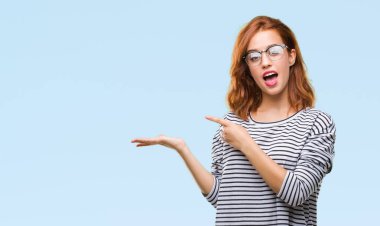 İzole arka plan hayrete ve el ile sunulması ve parmak ile işaret ederken kameraya gülümseyen gözlüklü genç güzel kadın.