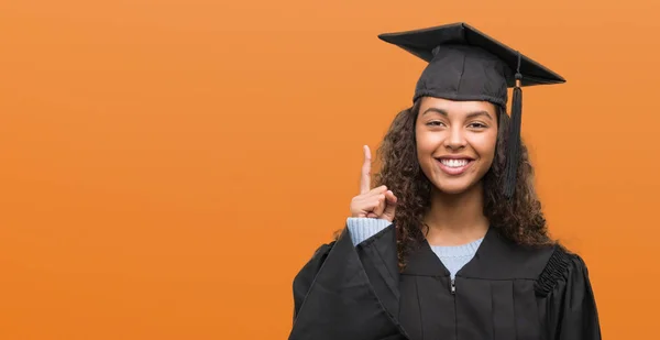 幸せそうな顔 ナンバーワンのアイデアや質問ポインティング指で卒業制服を着た若いヒスパニック女性を驚かせた — ストック写真