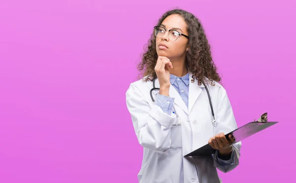 Joven Doctora Hispana Sosteniendo Portapapeles Cara Seria Pensando Pregunta Idea — Foto de Stock