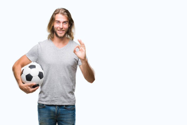 Young handsome man with long hair over isolated background holding football ball doing ok sign with fingers, excellent symbol