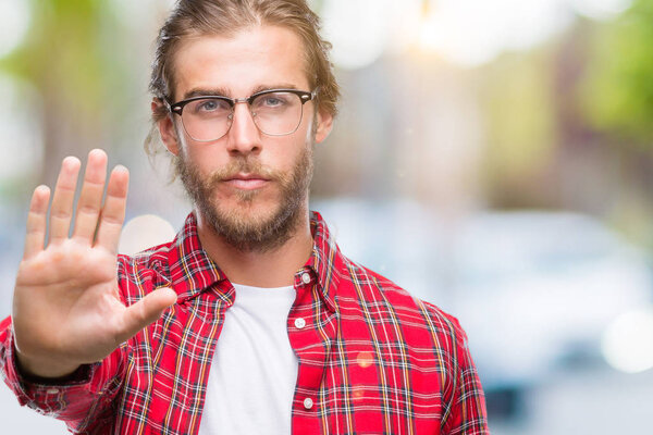 Молодой красивый мужчина с длинными волосами в очках на изолированном фоне делает остановку петь с ладонью руки. Предупреждающее выражение с негативным и серьезным жестом на лице
.