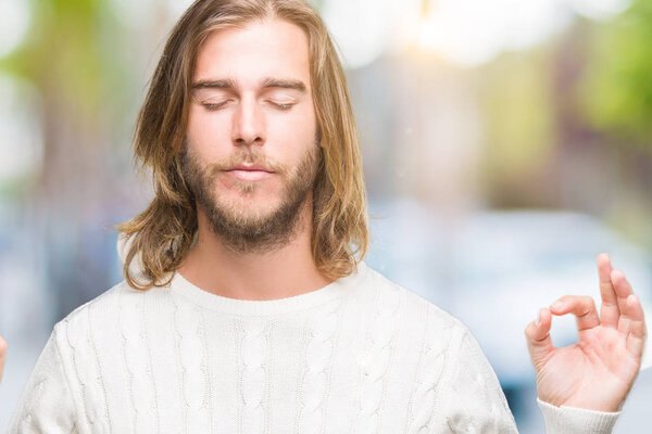 Young handsome man with long hair wearing winter sweater over isolated background relax and smiling with eyes closed doing meditation gesture with fingers. Yoga concept.