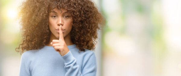 Африканская американка в свитере просит тишины с пальцем на губах. Молчание и тайная концепция
.