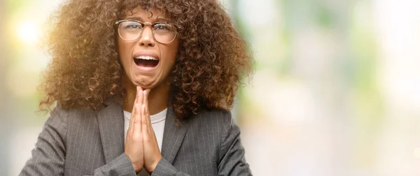 African american business woman wearing glasses begging and praying with hands together with hope expression on face very emotional and worried. Asking for forgiveness. Religion concept.