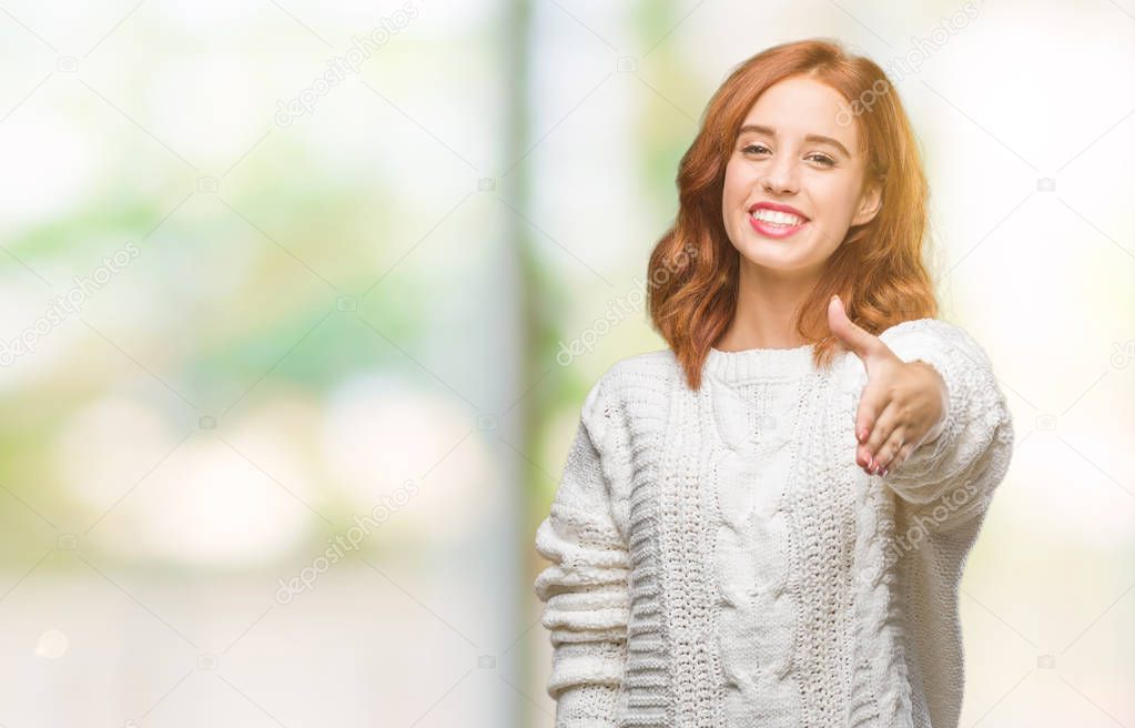 Young beautiful woman over isolated background wearing winter sweater smiling friendly offering handshake as greeting and welcoming. Successful business.