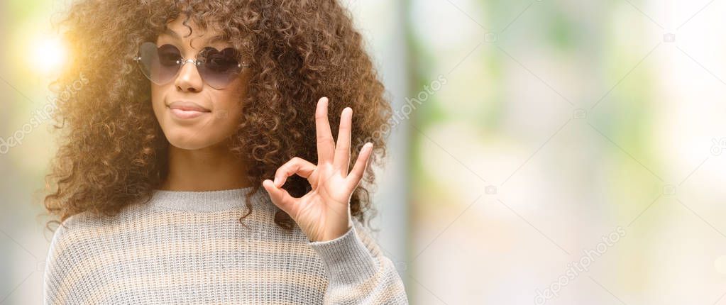 African american woman wearing a stripes sweater doing ok sign with fingers, excellent symbol