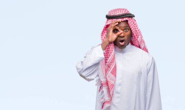 Sürpriz yüz, göz parmaklarının arasından seyir ile geleneksel keffiyeh ok jest yapıyor izole arka plan üzerinde giyen genç Arapça Afrika adam şok. İmansız ifade.