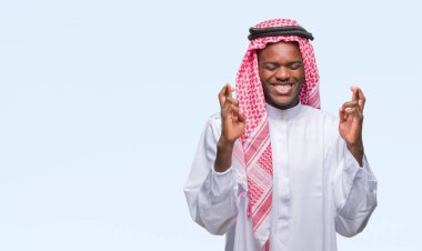 Geleneksel keffiyeh geçiş parmakları umut ve gözleri kapalı ile gülümseyen izole arka plan üzerinde giyen genç Arapça Afrika adam. Şans ve batıl kavramı.