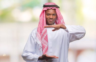 Geleneksel keffiyeh ile büyük ve büyük boy işaret, ölçü birimi sembol gösteren el eller izole arka plan üzerinde giyen genç Arapça Afrika adam. Kameraya bakarak gülümsüyordu. Ölçüm kavramı.