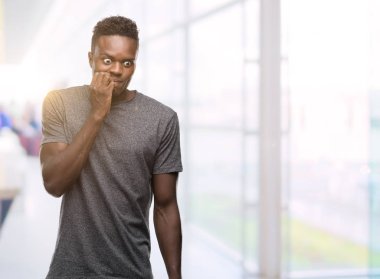 Stresli ve gergin elle çivi ısırma ağzına seyir gri t-shirt giyen genç Afro-Amerikan adam. Anksiyete sorunu.