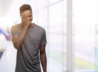 El yüz ve sürpriz duygu kendinden emin gülümseme ile tek gözü kaplayan gri t-shirt giyen genç Afro-Amerikan adam.