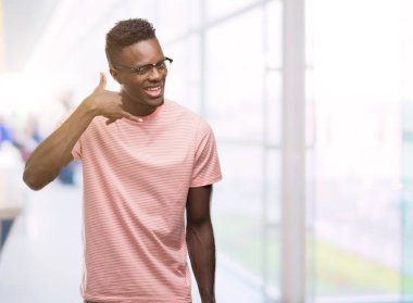 Pembe t-shirt giyen genç Afro-Amerikan erkek gülümseyen el ve parmak telefonda konuşmak ile telefon jest yapıyor. Kavramları iletişim.