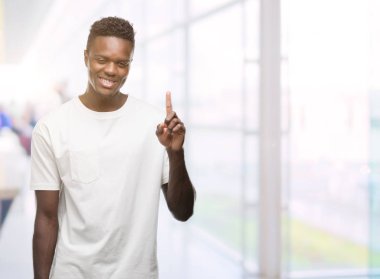 Gösterilen ve kendinden emin ve mutlu gülümseyen bir parmak ile işaret eden oktan yukarı beyaz t-shirt giyen genç Afro-Amerikan adam.