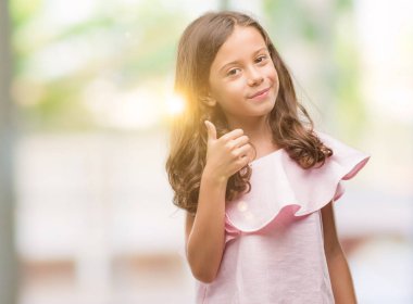 Hareketi el ile mutlu yaşasın yapıyor pembe elbise esmer Latin kız. Kameraya bakarak başarı gösteren ile ifade onaylama.