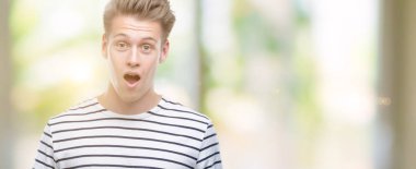 Genç yakışıklı sarışın adam giyen çizgili tişört korkuyor şok sürpriz yüz, denizci korkuyor ve heyecanlı korku ifadesi ile