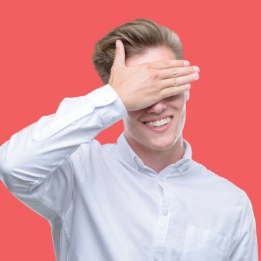 Gülümsüyor ve gözleri için sürpriz kapsayan yüz el ile gülüyor genç yakışıklı sarışın adam. Kör kavramı.