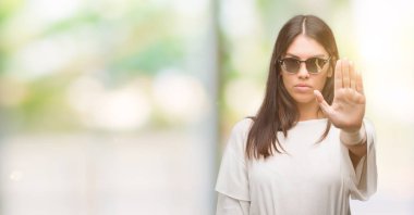 Genç güzel İspanyol açık eliyle dur işareti ile ciddi ve kendine güvenen ifade, savunma hareketi yaparken güneş gözlüğü takıyor