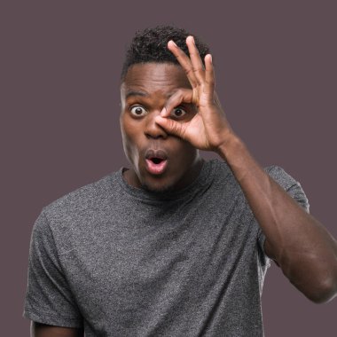 Sürpriz yüz, göz parmaklarının arasından seyir ile ok jest yapıyor gri t-shirt giyen genç Afro-Amerikan adam şok. İmansız ifade.