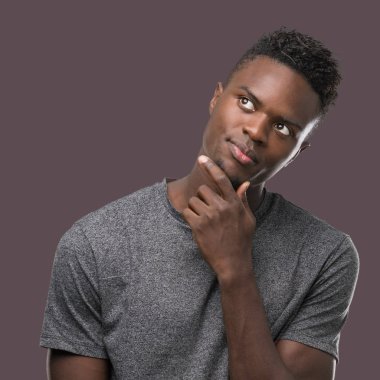 Çene düşünme hakkında soru, dalgın ifade üzerine el ile gri t-shirt giyen genç Afro-Amerikan adam. Düşünceli yüzüyle gülümsüyor. Şüphe kavramı.