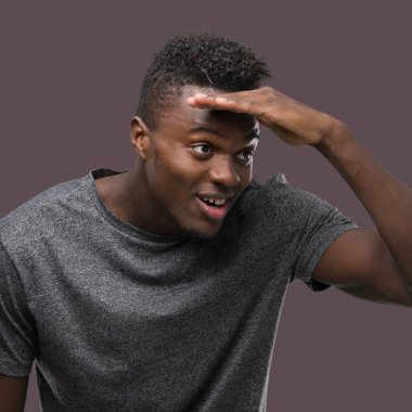 Çok mutlu ve gülümseyen uzakta el ile üzerine kafa seyir gri t-shirt giyen genç Afro-Amerikan adam. Arama kavramı.