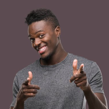 Gri t-shirt işaret parmakları için fotoğraf makinesi ile mutlu ve komik yüz giyen genç Afro-Amerikan adam. İyi enerji ve vibes.