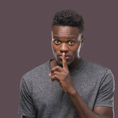 Dudaklarında parmak ile sessiz olmanı gri t-shirt giyen genç Afro-Amerikan adam. Sessizlik ve gizli kavramı.