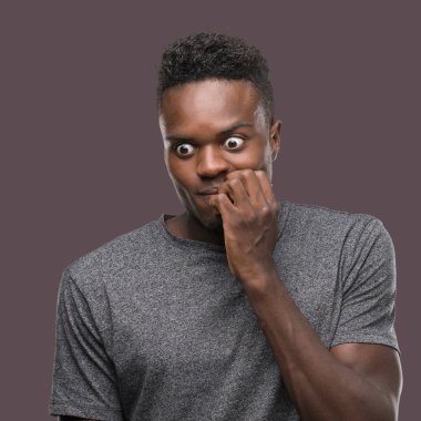 Stresli ve gergin elle çivi ısırma ağzına seyir gri t-shirt giyen genç Afro-Amerikan adam. Anksiyete sorunu.