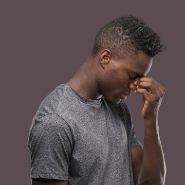 Gri t-shirt yorgun sürtünme burun ve göz yorgunluğu ve baş ağrısı duygu giyen genç Afro-Amerikan adam. Stres ve hayal kırıklığı kavramı.